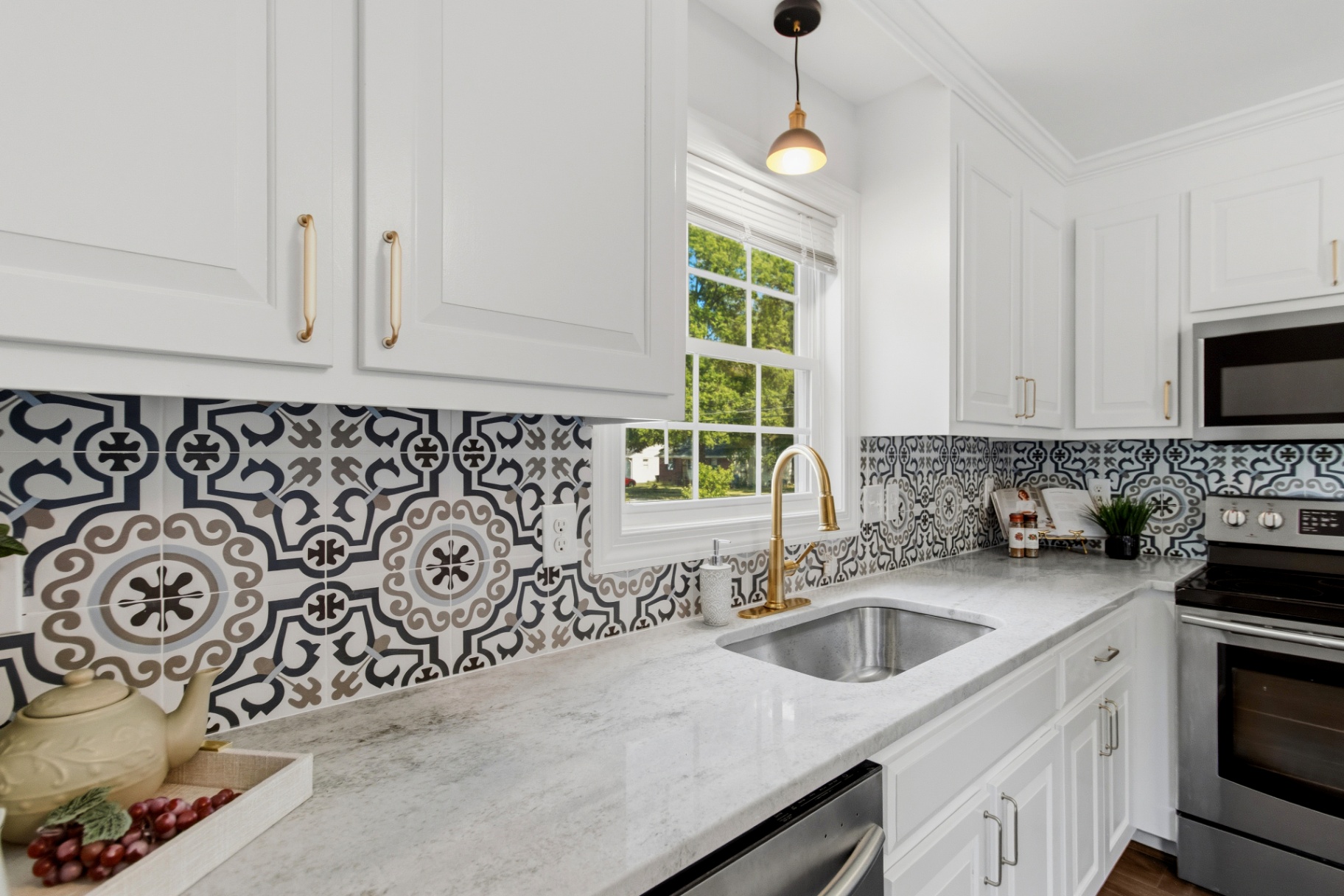 Close-up of white kitchen with marble counters, brass faucet, and Moroccan-style backsplash