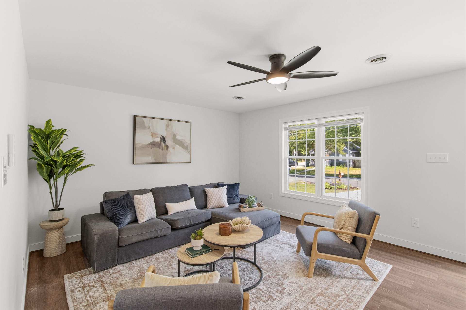 Staged living room with gray sectional, neutral rug, and warm hardwood floors