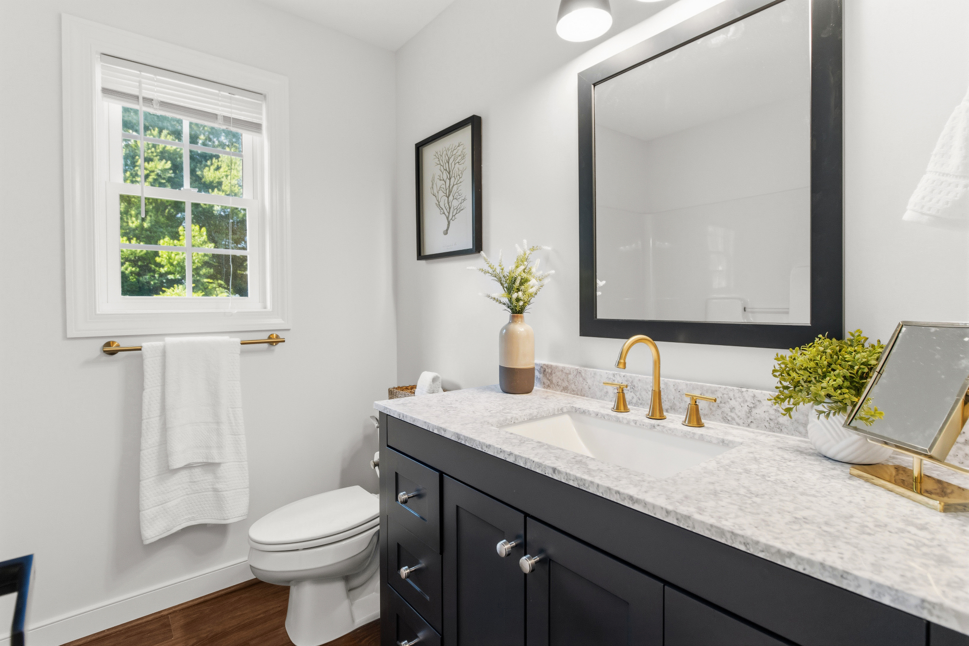 Updated bathroom with dark vanity, brass faucet, and marble-look countertop