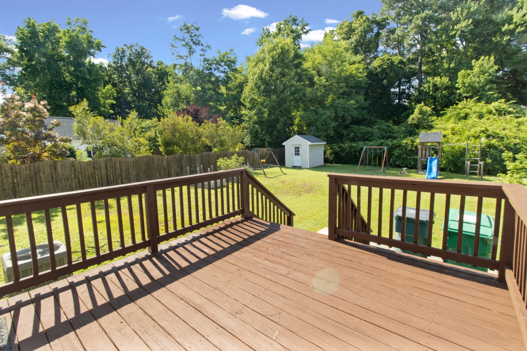 Back deck overlooking a large fenced yard with play area and storage shed